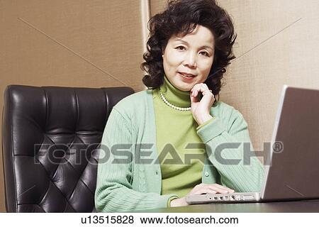 Portrait of a businesswoman sitting in front of a laptop smiling View Large Photo Image Stock Photo - Portrait of a businesswoman sitting in front of a laptop smiling. Fotosearch