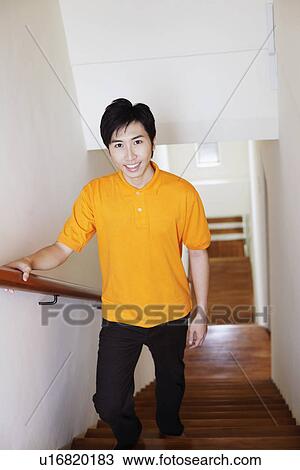 Stock Image - Portrait of a young man walking up stairs and smiling. Fotosearch