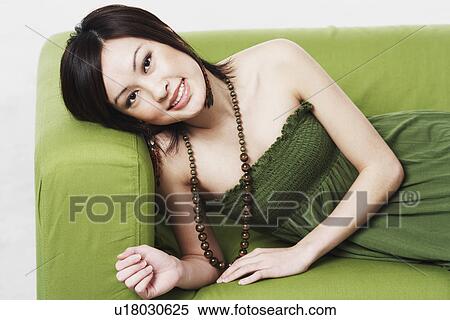 Stock Photography - Portrait of a young woman lying on a couch smiling. Fotosearch