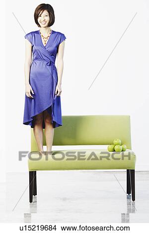 Picture - Portrait of a young woman standing on a couch. Fotosearch