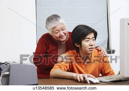 Close-up of a grandson using a computer with his grandmother standing behind him View Large Photo Image Stock Photography - Close-up of a grandson using a computer with his grandmother standing behind him. Fotosearch