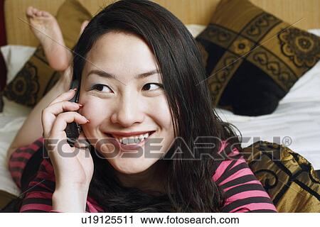 Close-up of a young woman lying on the bed using a mobile phone View Large Photo Image Stock Image - Close-up of a young woman lying on the bed using a mobile phone. Fotosearch