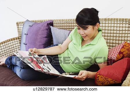Stock Photo - Close-up of a young woman reclining on a couch and reading a newspaper. Fotosearch