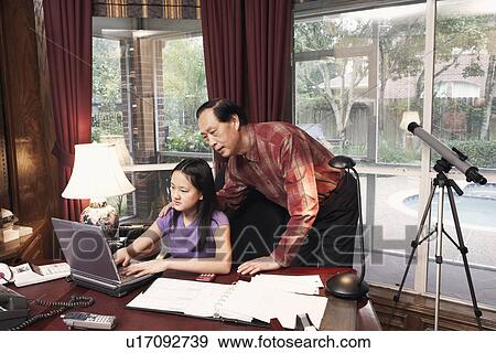 Stock Photo - Girl using a laptop with her grandfather standing beside her. Fotosearch