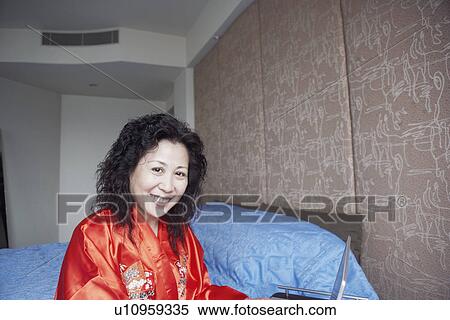 Stock Photography - Portrait of a mature woman sitting on the bed smiling. Fotosearch