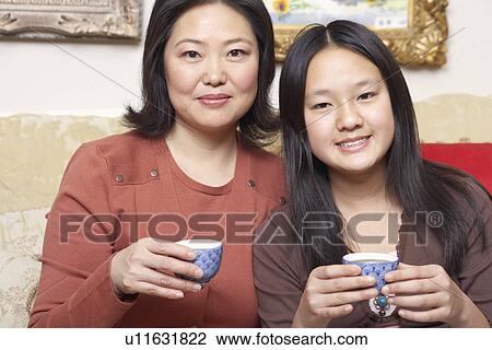 Stock Image - Portrait of a mother and her daughter holding tea cups. Fotosearch