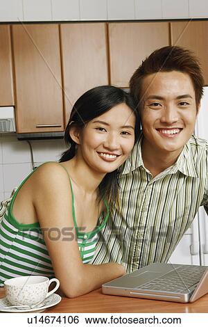 Stock Photograph - Portrait of a young couple smiling in front of a laptop at a kitchen counter. Fotosearch