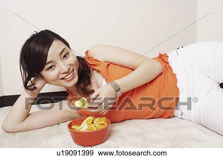 Portrait of a young woman lying on her side holding a slice of orange View Large Photo Image Stock Photo - Portrait of a young woman lying on her side holding a slice of orange. Fotosearch