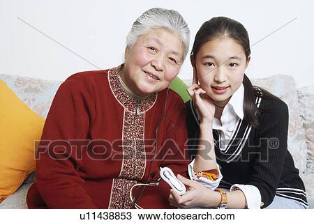 Stock Image - Portrait of a young woman sharing headphones with her grandmother. Fotosearch