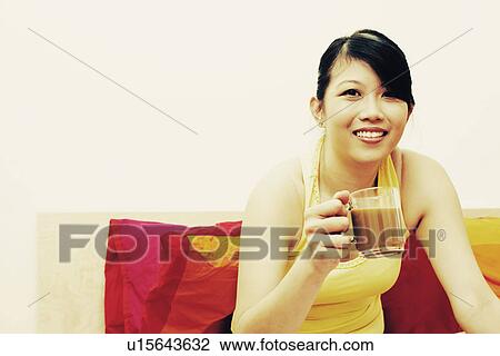 Stock Image - Portrait of a young woman smiling and holding a cup of coffee. Fotosearch