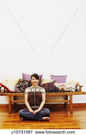 Stock Photo - Portrait of a young woman smiling and sitting on a hardwood floor. Fotosearch