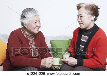 Side profile of a senior woman sitting on a couch with a mature woman holding tea cups View Large Photo Image Stock Photograph - Side profile of a senior woman sitting on a couch with a mature woman holding tea cups. Fotosearch