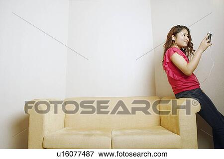 Stock Photo - Side profile of a young woman looking at an MP3 player. Fotosearch