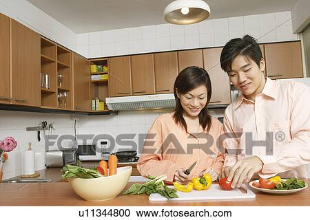 Stock Image - Young couple cutting vegetables at a kitchen counter. Fotosearch