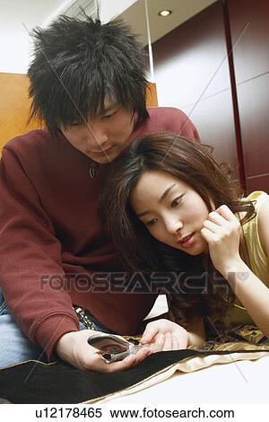 Stock Photography - Young couple lying on the bed holding a mobile phone. Fotosearch