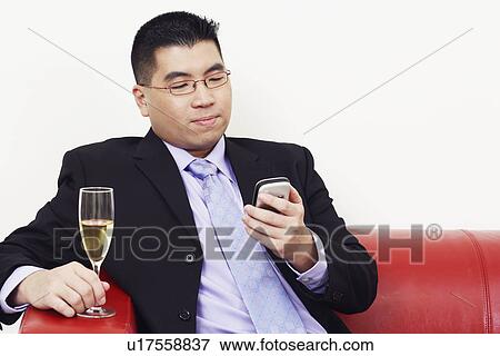 Stock Photo - Close-up of a businessman holding a champagne flute and operating a mobile phone. Fotosearch