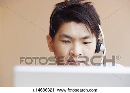 Stock Image - Close-up of a male customer service representative talking on a headset and using a laptop. Fotosearch