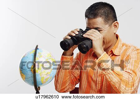 Close-up of a mid adult man looking at a desktop globe through a pair of binoculars View Large Photo Image Stock Image - Close-up of a mid adult man looking at a desktop globe through a pair of binoculars. Fotosearch