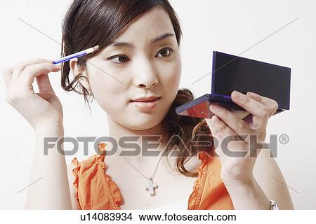 Picture - Close-up of a young woman holding a make-up brush and a hand mirror. Fotosearch