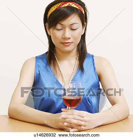 Stock Image - Close-up of a young woman holding a glass of wine with her eyes closed. Fotosearch