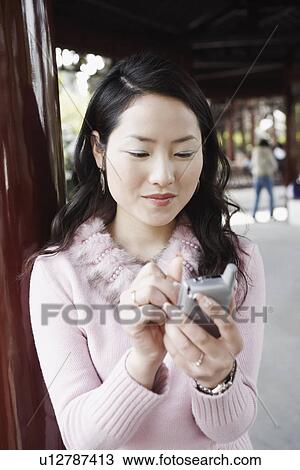Stock Image - Close-up of a young woman operating a mobile phone with a digitized pen smiling. Fotosearch