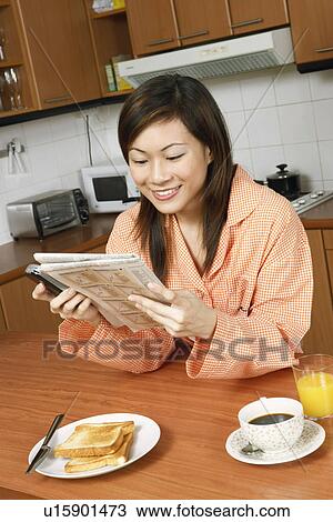 Stock Image - Close-up of a young woman reading a newspaper at a kitchen counter. Fotosearch
