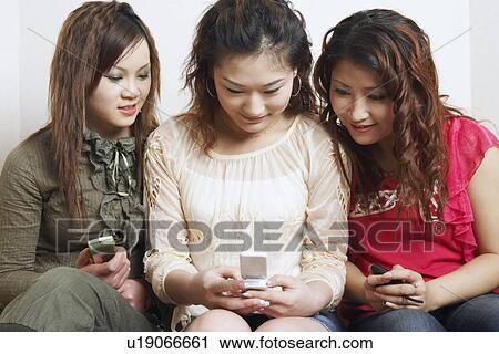 Stock Image - Close-up of three young women looking at a mobile phone. Fotosearch