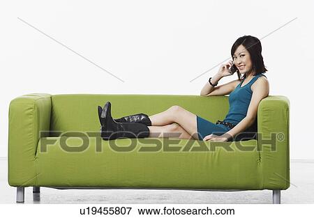 Portrait of a young woman sitting on a couch talking on a mobile phone View Large Photo Image Stock Photo - Portrait of a young woman sitting on a couch talking on a mobile phone. Fotosearch