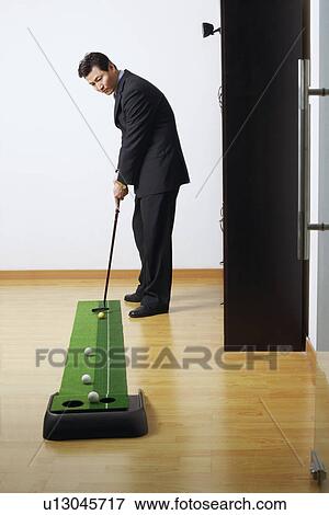 Stock Photo - Side profile of a businessman practicing golf in a club. Fotosearch