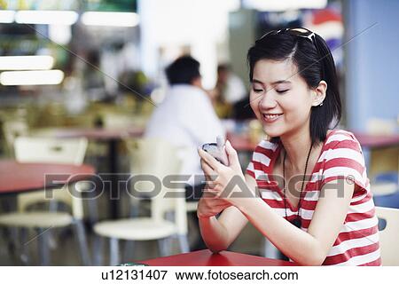 Side profile of a young woman sitting in a restaurant and using a mobile phone View Large Photo Image Stock Photo - Side profile of a young woman sitting in a restaurant and using a mobile phone. Fotosearch