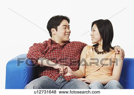 Stock Photo - Close-up of a young couple sitting on a couch looking at each other. Fotosearch