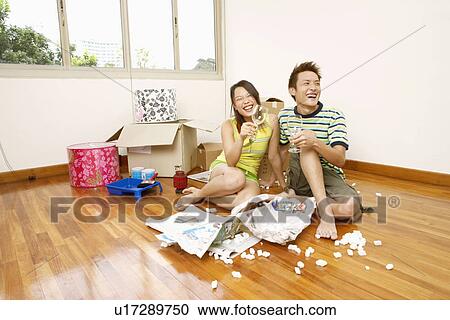 Stock Image - Close-up of a young couple sitting on the floor and holding wineglasses. Fotosearch