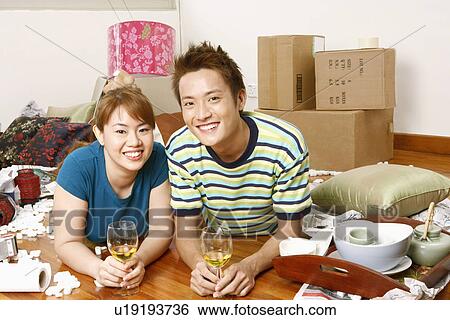 Stock Photograph - Portrait of a young couple lying on the floor and holding glasses of wine. Fotosearch
