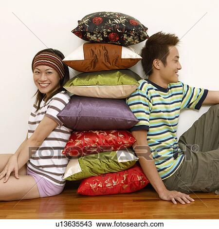 Stock Image - Portrait of a young couple sitting and leaning against a stack of cushions. Fotosearch