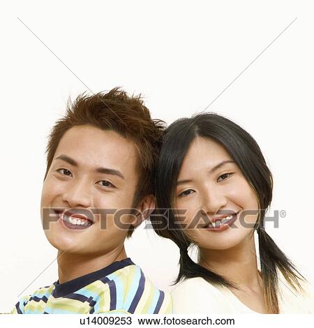 Stock Image - Portrait of a young couple sitting back to back and smiling. Fotosearch