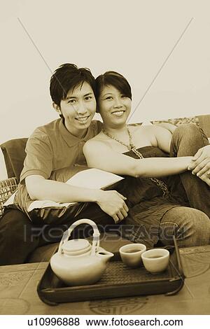Stock Photo - Portrait of a young couple smiling and sitting on a couch. Fotosearch