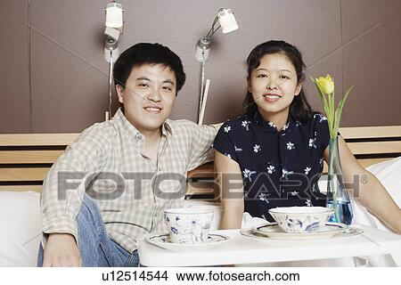 Portrait of a young man and a mid adult woman sitting on the bed View Large Photo Image Picture - Portrait of a young man and a mid adult woman sitting on the bed. Fotosearch