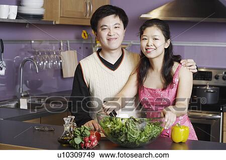 Stock Photo - Portrait of a young man standing with a mid adult woman in the kitchen. Fotosearch