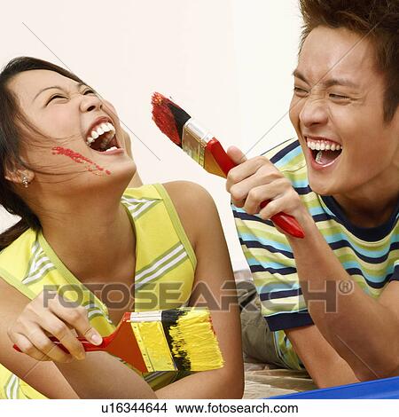 Picture - Young couple holding paintbrushes and laughing. Fotosearch