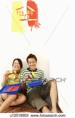 Stock Image - Young couple holding paintbrushes and looking cheerful. Fotosearch