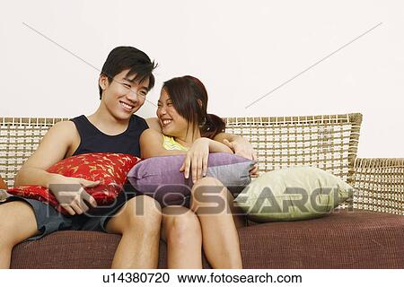 Stock Image - Young couple sitting on a couch and smiling. Fotosearch