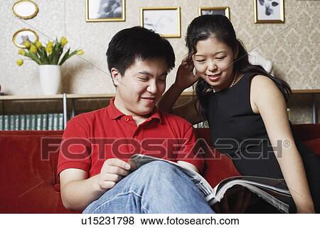 Young couple sitting on a couch reading a magazine View Large Photo Image Stock Photo - Young couple sitting on a couch reading a magazine. Fotosearch