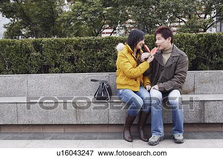 Stock Photo - Young couple sitting on the ledge eating watermelon. Fotosearch