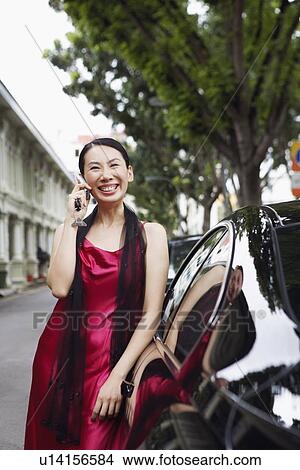 Picture - Businesswoman leaning against a car and talking on a mobile phone. Fotosearch