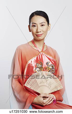 Stock Image - Portrait of a mid adult woman holding a folding fan and smiling. Fotosearch