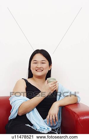 Stock Image - Portrait of a mid adult woman sitting on a couch and holding a tea cup. Fotosearch