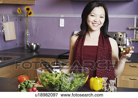Stock Photo - Portrait of a young woman holding a wineglass smiling in the kitchen. Fotosearch