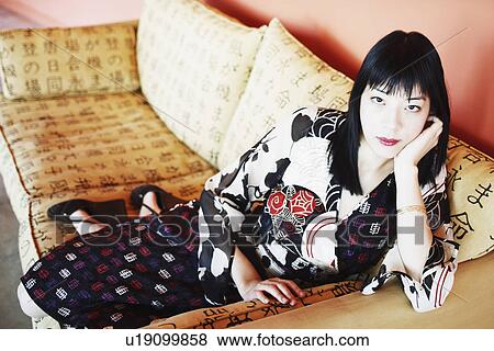 Stock Photo - Portrait of a young woman leaning on a couch. Fotosearch