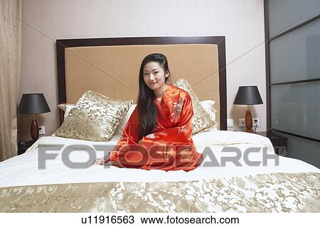 Stock Image - Portrait of a young woman sitting on the bed smiling. Fotosearch