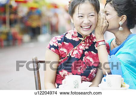 Picture - Close-up of a young woman whispering into another woman's ear. Fotosearch